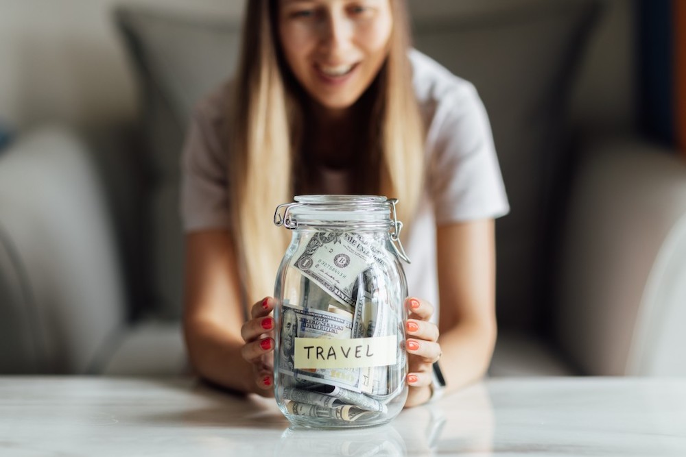 Image of a woman in front of a jar of money labeled "travel"