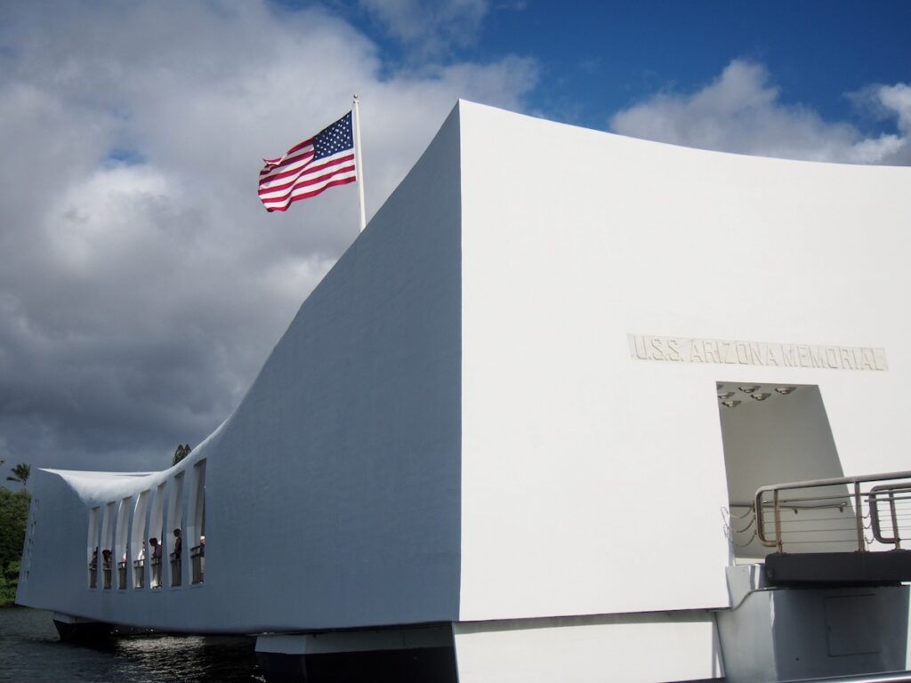 Image of An American flag flys over the Arizona Memorial where the USS Arizona was sunk during the attack on Pearl Harbor on Oahu Hawaii.