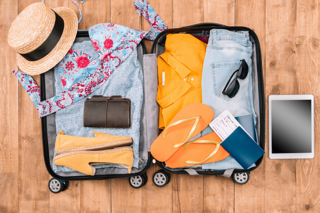 Image of an open suitcase with flip flops, sunglasses, clothing, hat, etc